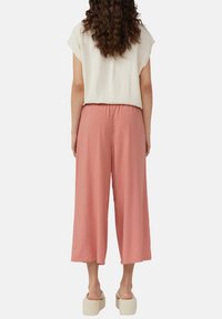 Lichtroze wijde broek met een elastische tailleband, gemaakt van lichte stof, gecombineerd met een ivoorkleurige top met korte mouwen.