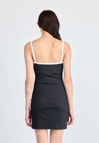 Zwarte bodycon jurk met dunne witte bandjes, met een gladde textuur en een strakker ontwerp. De achterkant is laag uitgesneden met minimale details.