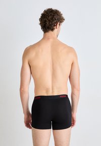 Black boxer shorts with red Hugo logo on the waistband, fitting close to the body, made from a smooth, stretchy material.