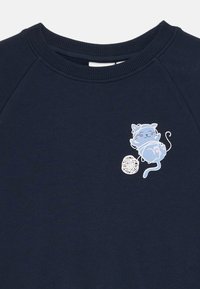 Sudadera azul marino con un gráfico de un gato blanco y azul claro, interactuando de forma juguetona con un ovillo de lana. Tejido suave y texturizado.