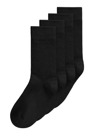 Quatre paires de chaussettes noires côtelées montantes empilées, avec une paire légèrement devant les autres sur fond blanc.
