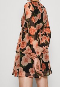 Blommig klänning med svart bakgrund och stora rosa rosor, långärmad, med smockad midja och lager av volanger vid fållen.