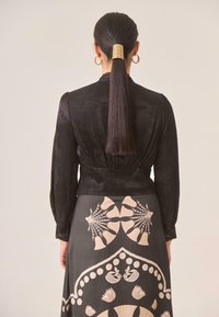 Chaqueta negra de manga larga con tejido texturizado combinada con una falda estampada que presenta diseños florales en tonos beige y rosa. Accesorio para el cabello dorado visible.
