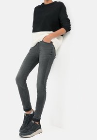 Suéter de punto en blanco y negro, jeans ajustados grises y zapatillas oscuras. El suéter tiene una textura acanalada, los jeans son ajustados y tienen bolsillos.