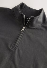 Maglione grigio con design a mezza zip, realizzato in tessuto liscio. Presenta un colletto alto e cuciture sottili lungo i bordi.