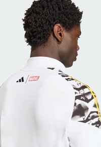 White athletic jacket featuring black and yellow accents, with Marvel logo, and graphic design on the sleeves. Soft texture and high collar.