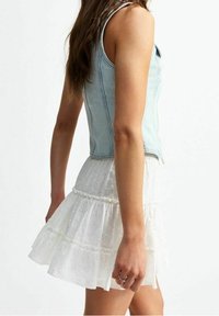 Haut sans manches en denim bleu clair associé à une mini-jupe blanche à volants superposés avec des détails en œillets et des accents de volants.