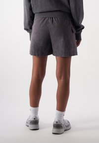 Schwarze Shorts aus einem weichen Stoff, mit einem elastischen Bund und seitlichen Taschen. Getragen mit grauen Turnschuhen und weißen Socken.