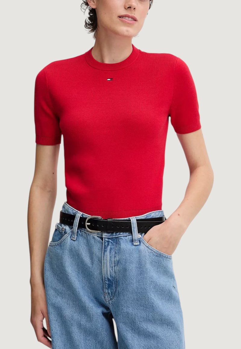 Maglietta rosso a maniche corte in maglia con scollo tondo, taglio aderente e un delicato logo sul petto. Abbinata a jeans blu a vita alta.