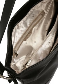 Interno di una borsa in pelle nera con una morbida fodera beige, due tasche con zip e delicate fantasie geometriche sul tessuto.