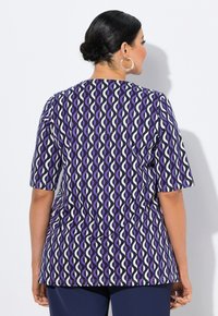 Top de color púrpura con estampado de diseños en ondas en blanco y azul oscuro, mangas cortas y un corte relajado. Textura de tela suave.