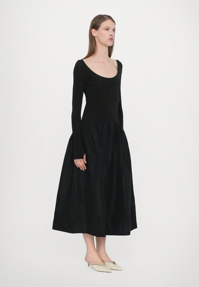 Vestido negro de manga larga con un cuerpo ajustado y una falda fluida. Hecho de una tela suave, presenta un escote redondeado y una cintura fruncida.