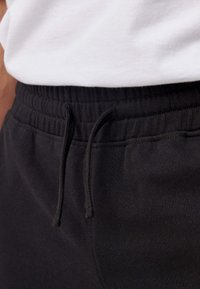 Zwarte joggerbroeken met een elastische tailleband en een trekkoorddetail, close-up weergave van de stiksels en stof.