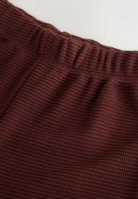 Burgundská tkanina s textúrou vaflí s elastickým pásom. Povrch má mriežkový vzor, ktorý ukazuje hlbokú, bohatú farebnú variáciu.