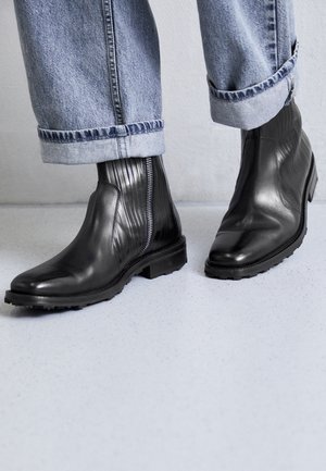 Zwarte leren enkellaarsjes met getextureerde ribbels en een zijrits. Dikke rubberen zolen en een afgeronde teen, gecombineerd met opgerolde denim.