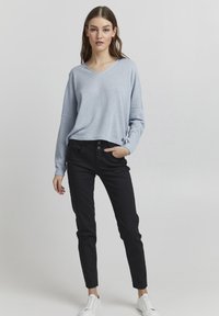 Pullover v-neck di colore azzurro chiaro con maniche lunghe, vestibilità rilassata. Abbinato a pantaloni neri slim-fit e sneakers bianche. Tessuto morbido, dettagli minimi.