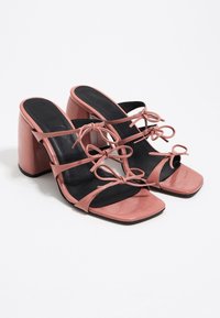 Sandales à talons hauts en cuir verni rose avec des orteils carrés, trois fines lanières avec des nœuds, et des semelles intérieures rembourrées noires.