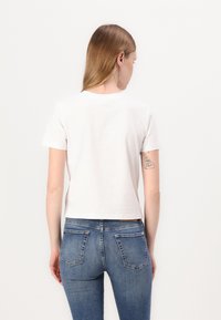 Tricou alb din bumbac cu mâneci scurte, design scurt, gât rotund, asociat cu blugi din denim albastru cu buzunare la spate și detalii spalate.