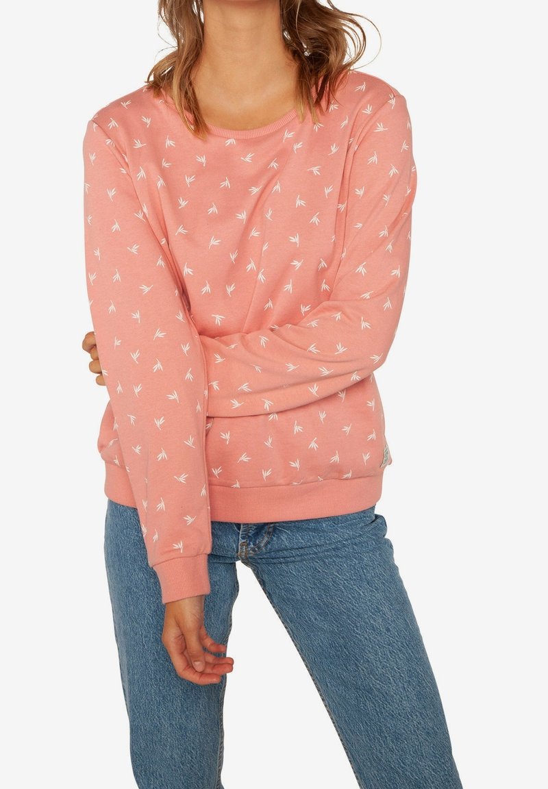 Sudadera rosa con patrones de hojas blancas, de mangas largas, cuello redondo y puños y bajo acanalados. Combinada con vaqueros azules.