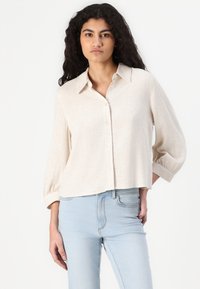 Lett beige knapp-up skjorte i teksturert stoff, med klassisk krage og trekvart ermer, kombinert med lyseblå bukser.