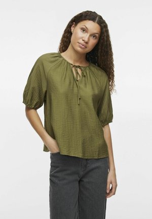Blusa de manga corta en verde oliva con un patrón texturizado, cuello con lazo y un corte relajado, combinada con pantalones de pierna ancha en gris oscuro.