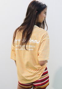 T-shirt surdimensionné rayé jaune et blanc avec du texte dans le dos, assorti à un short en crochet rayé multicolore. Tissu lisse, coupe décontractée.