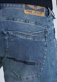 Modré džíny z denimu s vybledlým povrchem, mají vyšitý zadní kapsu, koženou nášivku s logem "PME LEGEND" a kovový detail na knoflíku.