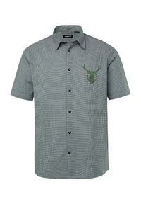 Camisa de manga corta y botones en patrón de cuadros en blanco y negro, con un emblema de cabeza de ciervo verde en el lado izquierdo del pecho. La tela parece ser de tipo tejido.