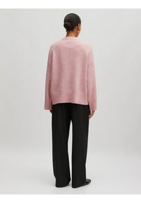 Rosa gestrickter Pullover mit lockerer Passform, überschnittenen Schultern und geripptem Saum, kombiniert mit weiten schwarzen Hosen. Glatte Textur und lässiges Design.