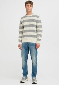 Cream sweater with black horizontal stripes, textured knit design, paired with light blue jeans and grey sneakers on a plain background.