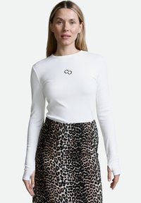 Weißes Langarmoberteil mit gerippter Textur und schwarzem Unendlichkeitslogo auf der Brust, kombiniert mit einem Rock im braunen und schwarzen Leopardenmuster.