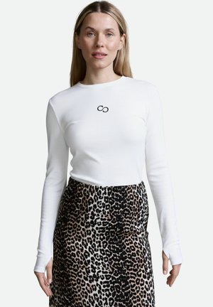 Weißes Langarmoberteil mit gerippter Textur und schwarzem Unendlichkeitslogo auf der Brust, kombiniert mit einem Rock im braunen und schwarzen Leopardenmuster.