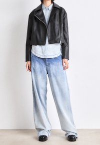 Giacca in pelle nera corta con zip, abbinata a una camicia in denim azzurro con bottoni e jeans larghi in denim blu sbiadito. Scarpe nere.