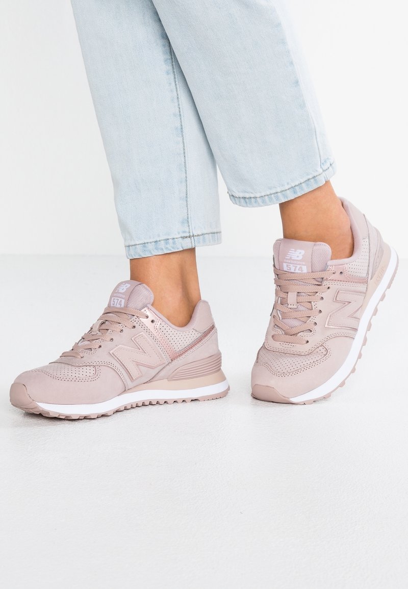 Vaaleanpunaiset New Balance -lenkkarit, joissa on hengittävä verkkorakenne, tekstuuriset suede-paneelit ja valkoinen kumipohja, jossa on numero 574.