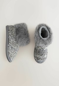 Grå strikkede tøfler med kunstpelskant, der har en tekstureret overflade og fleksible gummisåler. Designet til indendørs komfort og varme.