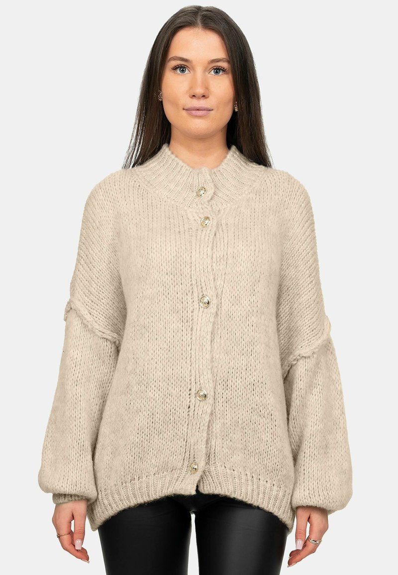 Cardigan beige lavorato a maglia con colletto alto, vestibilità oversize e grandi bottoni, caratterizzato da polsini e orlo a costine per texture e dettagli.