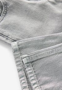 Tessuto di denim grigio con una texture liscia. Le caratteristiche includono cuciture visibili e una leggera lucentezza, con un bordo piegato che mostra i dettagli interni.