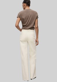 Brown short-sleeved shirt, fitted at shoulders. Off-white, high-waisted, wide-leg pants with two back pockets and frayed hem.