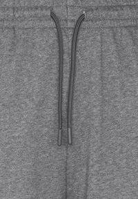 Pantalon de survêtement gris avec taille à cordon, présentant une texture douce et des poignets élastiques. Accents notables de cordon noir à la taille.