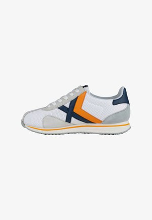Zapatilla atlética blanca de malla con acentos en gris y azul marino, que presenta una franja naranja y un panel de ante gris texturizado. Diseño con cordones y suela de goma.