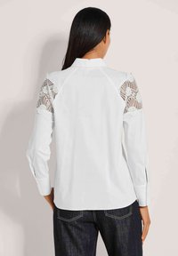 Witte shirt met kanten accenten op de schouders, lange mouwen met manchetten en een klassieke kraagontwerp.