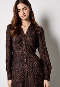 Abito nero con stampa leopardata marrone, chiusura a bottoni frontale, maniche lunghe e dettagli arricciati sul petto. Tessuto di texture liscia.