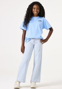 Camiseta de algodón de color azul claro con "Good Days" impreso en negro, combinada con jeans acampanados de patrón azul claro y zapatillas blancas.