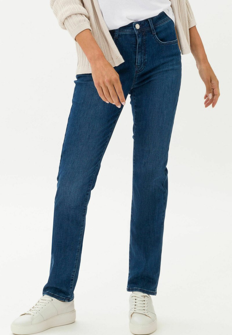Dunkelblaue Denim-Jeans mit geradem Bein, ausgestattet mit Fronttaschen, einem Gürtelschlaufen und einem Knopfverschluss. Getragen mit weißen Sneakern.