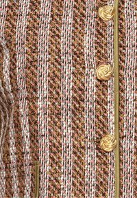 Tissu en tweed tissé avec des fils roses, marron et blancs, orné de boutons dorés torsadés en forme de corde et de passepoil vert olive sur un vêtement.