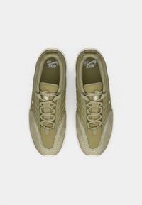 Ζεύγος ελιάς Nike SB αθλητικών παπουτσιών με λευκές σόλες και κορδόνια, απεικονιζόμενο από πάνω σε λευκό φόντο.