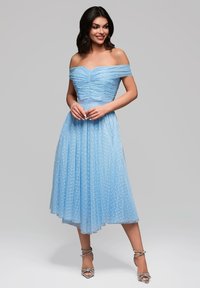 Ljusblå av-axeln-klänning med rynkad bodice, plisserad kjol och texturerade prickar, som matchas med silverfärgade remsandaler.