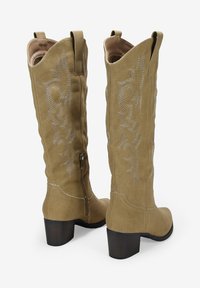 Botas altas de ante en color marrón claro, con costuras decorativas, puntera afilada y tacón cuadrado. Incluyen una cremallera lateral para facilitar su uso.