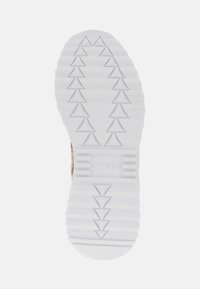 Semelle de sneaker blanche en caoutchouc texturé, avec un motif triangulaire et le logo "GUESS" en relief. Le design présente des stries pour une meilleure traction.
