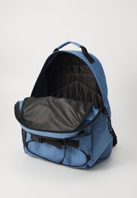 Blauer Rucksack mit strapazierfähigem äußeren Material, geräumigem Fach und schwarzem gepolstertem Innenraum. Verfügt über verstellbare Trageriemen und eine seitliche Netztasche.
